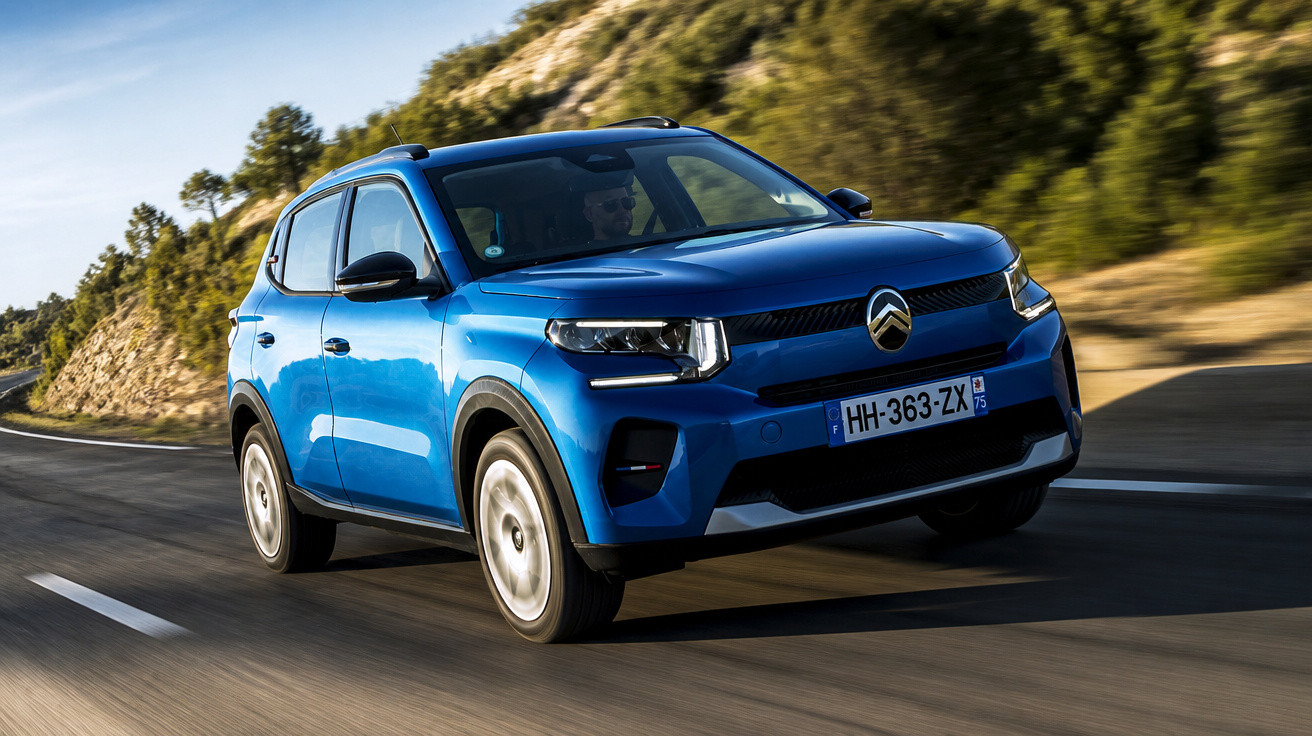 SUV Citroën bleu roulant sur une route de montagne au soleil, entouré de végétation.